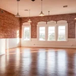 Empty event space with exposed brick walls, arched windows, wood floors and pendant lighting at The Electric Loft